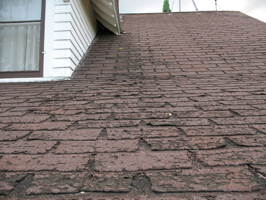 Asphalt shingles with bald spots from impact damage, weather, or poor maintenance