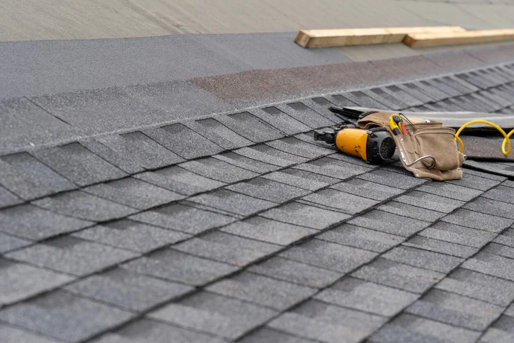 A nail gun rests on its side on an asphalt shingle roof