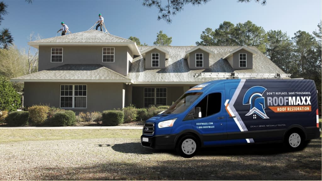 Two Roof Maxx dealers spray the treatment onto a customer's home behind a branded Roof Maxx van