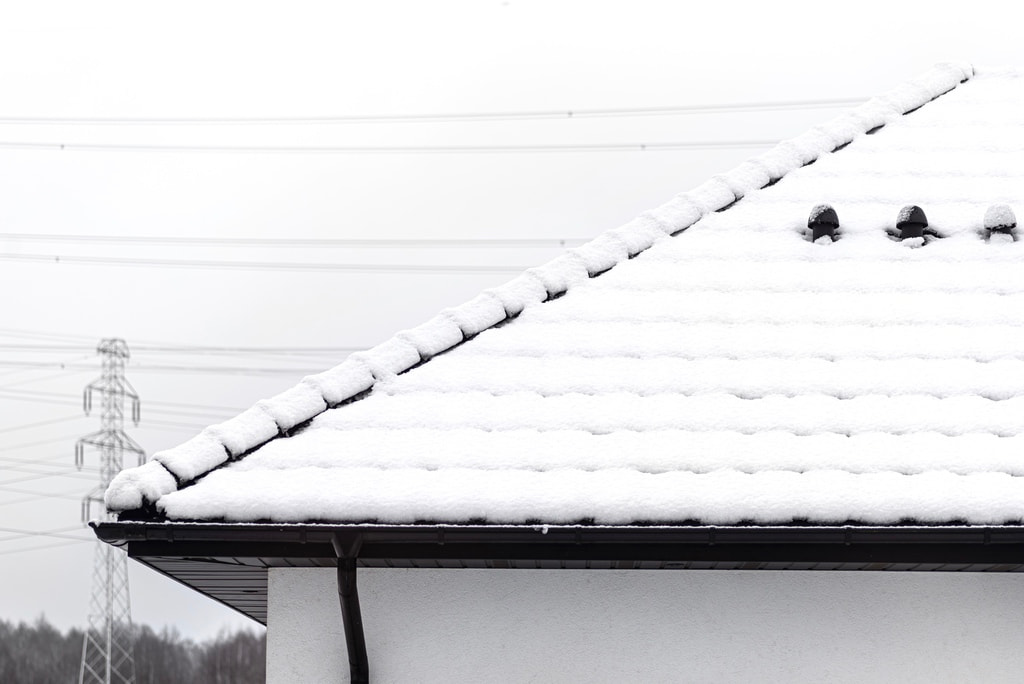 Side view of a snowy tile roof with black soffit