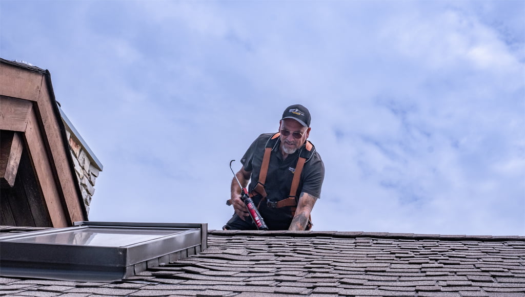 A roofer stands on a roof above skylight flashing.