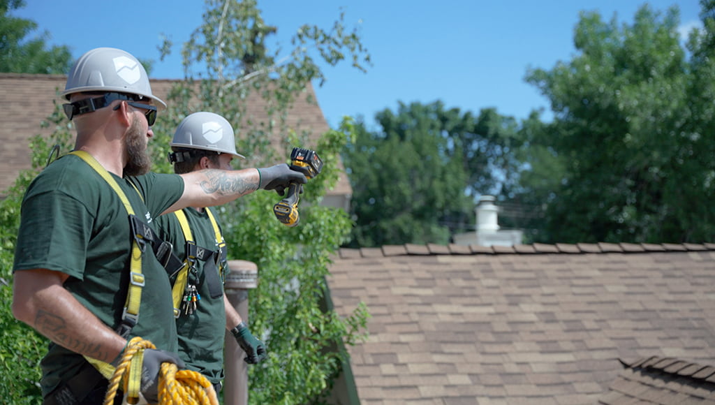 Two roofers inspect a roof before tackling a flashing repair job.