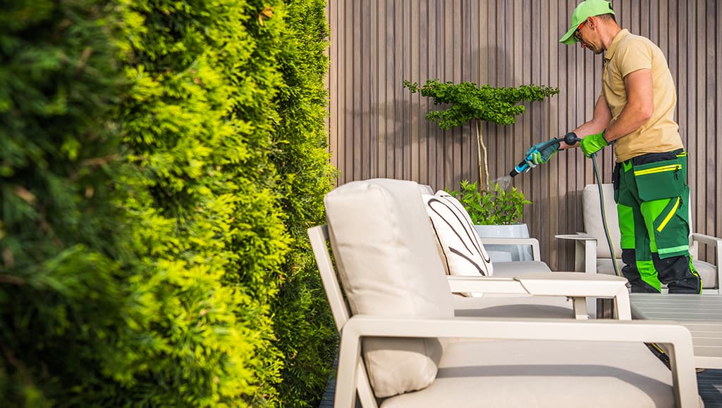 A maintenance man takes care of plants on a patio.