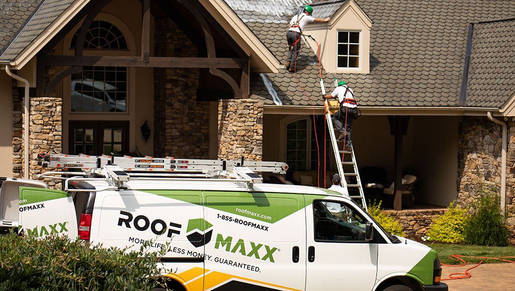 Two Roof Maxx dealers apply the treatment to an asphalt shingle roof. A Roof Maxx truck is in the foreground.