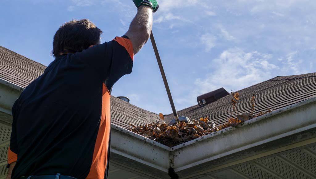 Homeowner cleaning debris from roof to protect shingles and extend shingle lifespan.