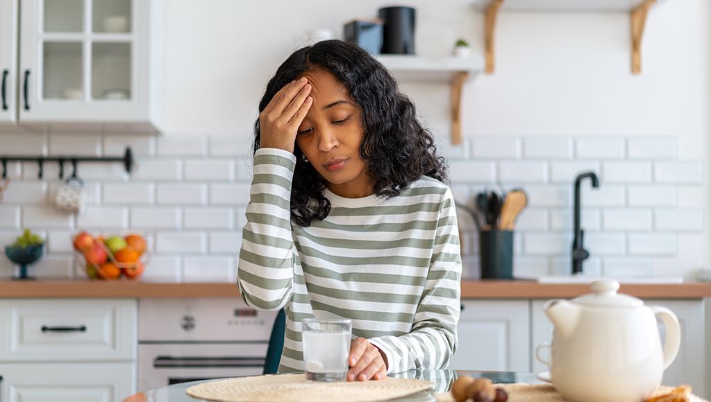 A woman stands in her kitchen treating a headache.