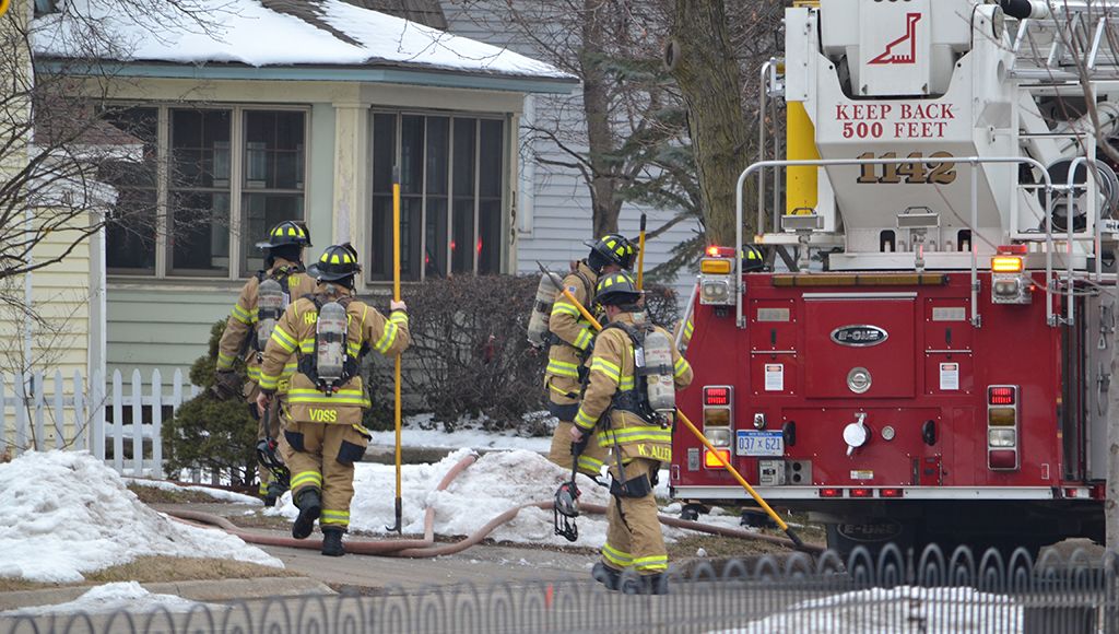 Firemen in uniforms arrive at a yellow house on a red and white firetruck