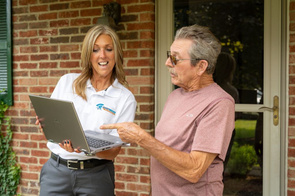 A Roof Maxx dealer shows a customer their roof score on a laptop computer.
