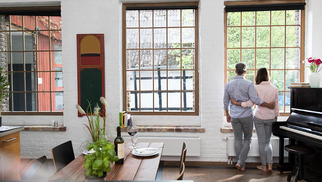 A man and woman stand in front of their single paned windows.