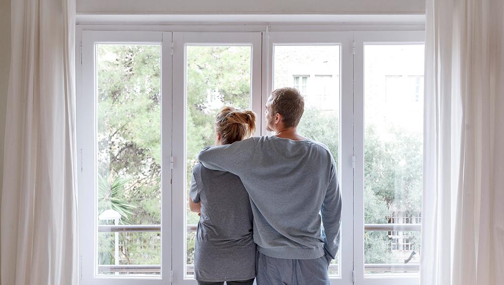 A man and woman stand looking out of a new set of double-paned windows.