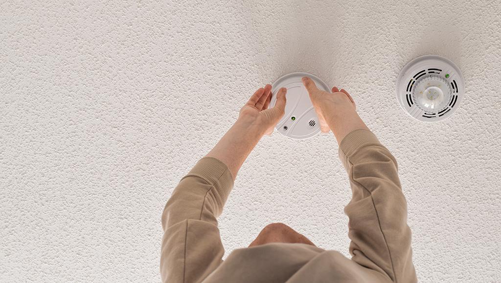 Man changing battery in a white smoke detector on the ceiling