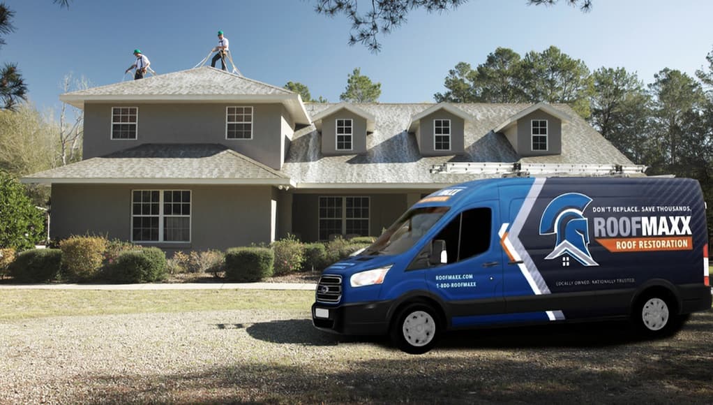 Two Roof Maxx dealers treat a residential roof. A blue branded Roof maxx van sits in the driveway.