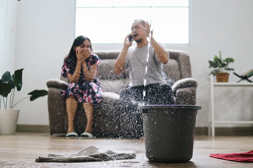 A man and his daughter look on in shock as water pours down from a leak in the roof.
