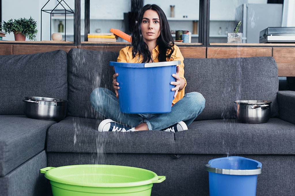 A woman uses colorful buckets to catch water in her living room