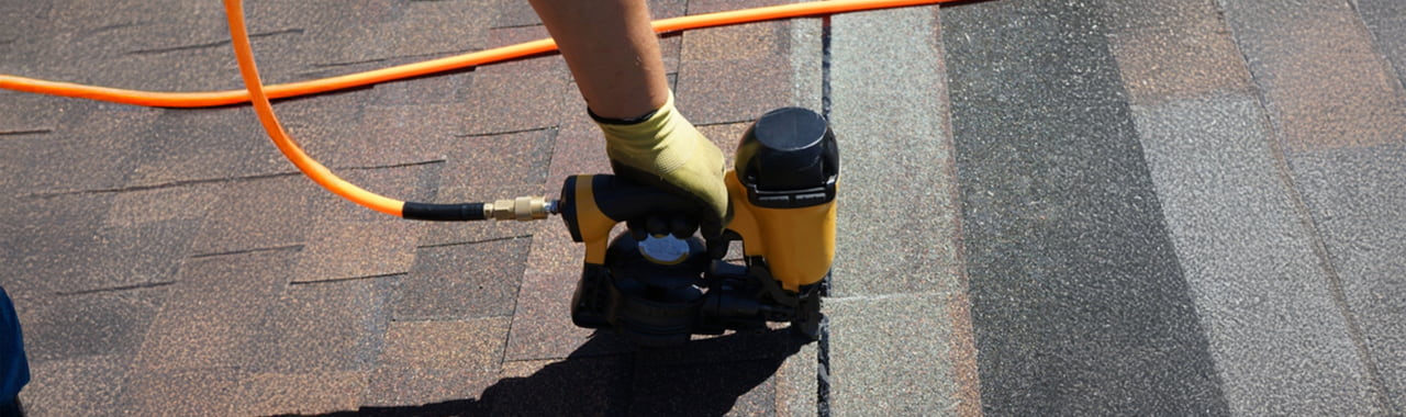 A roofer nailing asphalt shingles with an air gun.